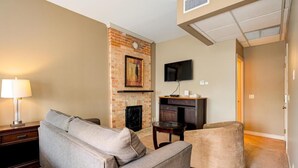 A living room with a fireplace, a flat-screen TV, and a sofa. - The Avonlea Inn (Stratford)