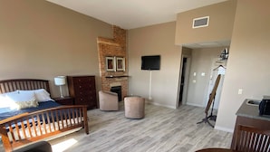 A spacious living area with a large bed, a fireplace, a television, and a dining table. - The Avonlea Inn (Stratford)