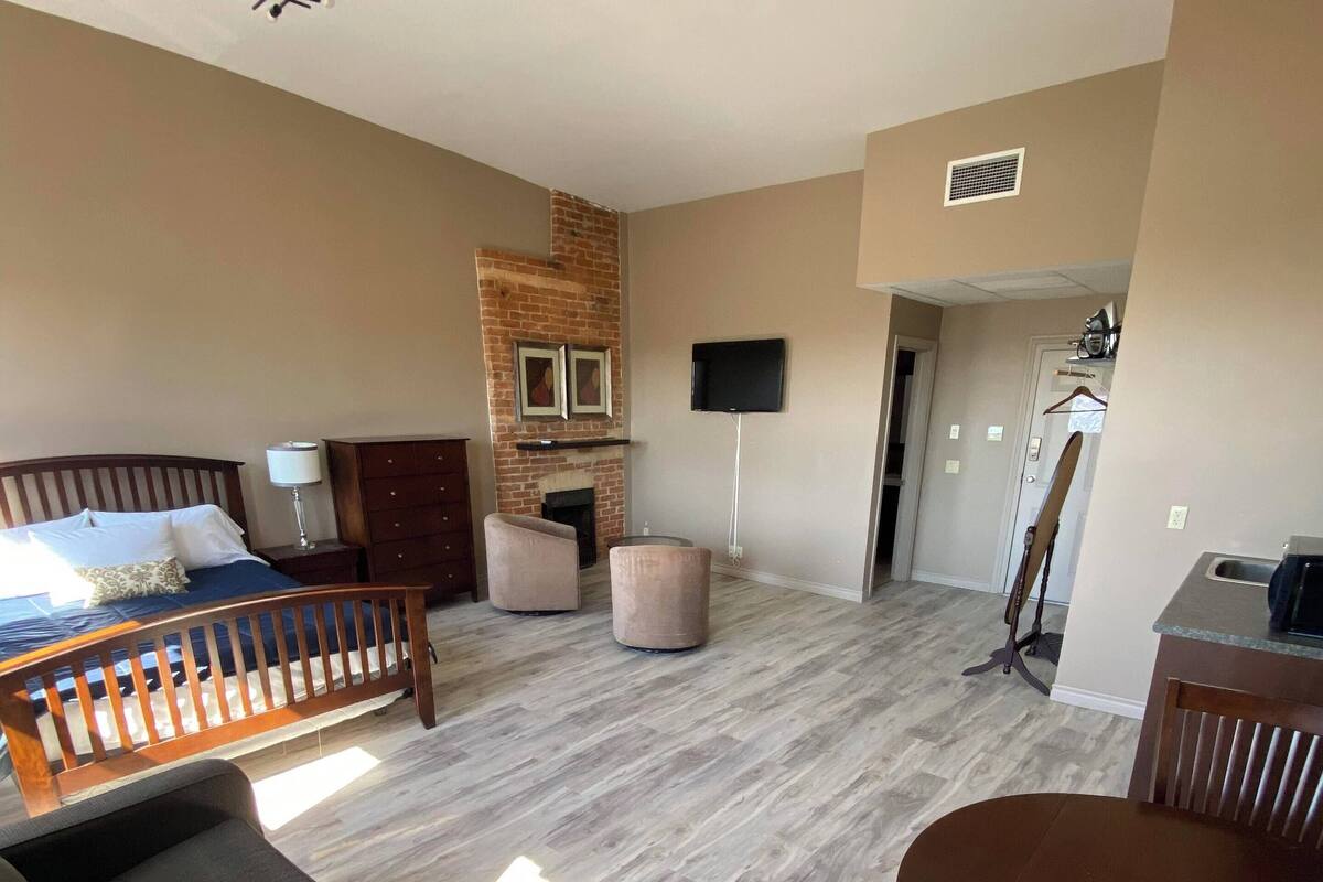 A spacious living area with a large bed, a fireplace, a television, and a dining table.