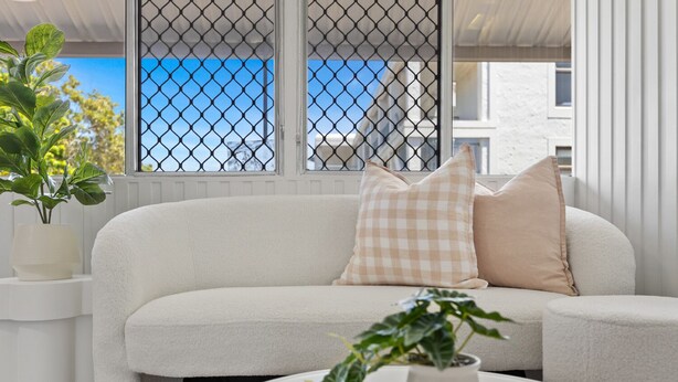 A white sofa with checkered pillows, a white coffee table, and a potted plant. - Cute & Compact, pet friendly apartment easy access to Alex or Mooloolaba beaches (Alexandra Headland)