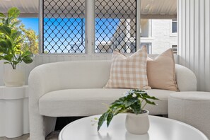 A white sofa with checkered pillows, a white coffee table, and a potted plant.