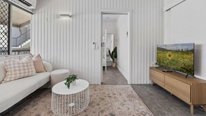 A modern living room with a white sofa, a round coffee table, and a TV on a wooden stand. - Cute & Compact, pet friendly apartment easy access to Alex or Mooloolaba beaches (Alexandra Headland)