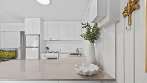 A modern kitchen with white cabinetry, a central island, and a decorative plant. - Cute & Compact, pet friendly apartment easy access to Alex or Mooloolaba beaches (Alexandra Headland)
