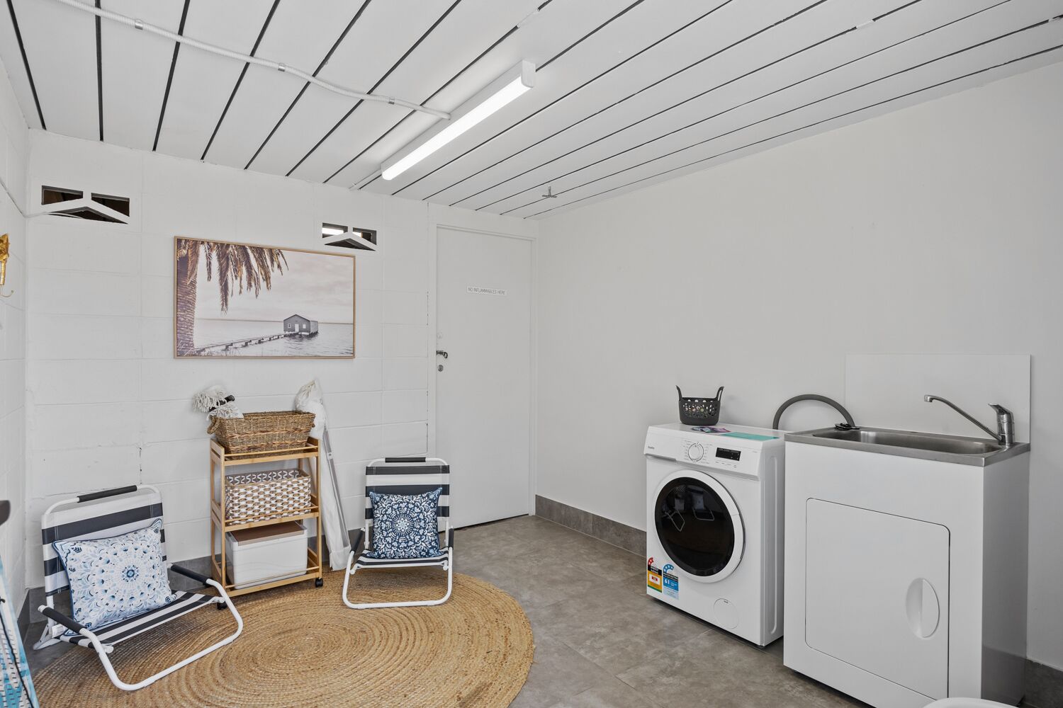 Un cuarto de lavandería con lavadora, lavamanos, tendedero y una silla.