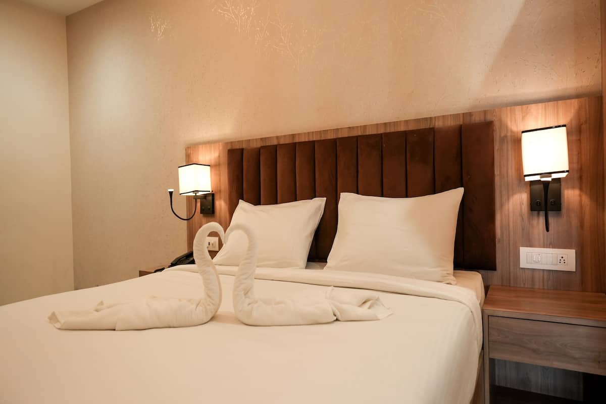Une chambre d’hôtel avec un grand lit, deux lampes fixées au mur et une tête de lit en bois.