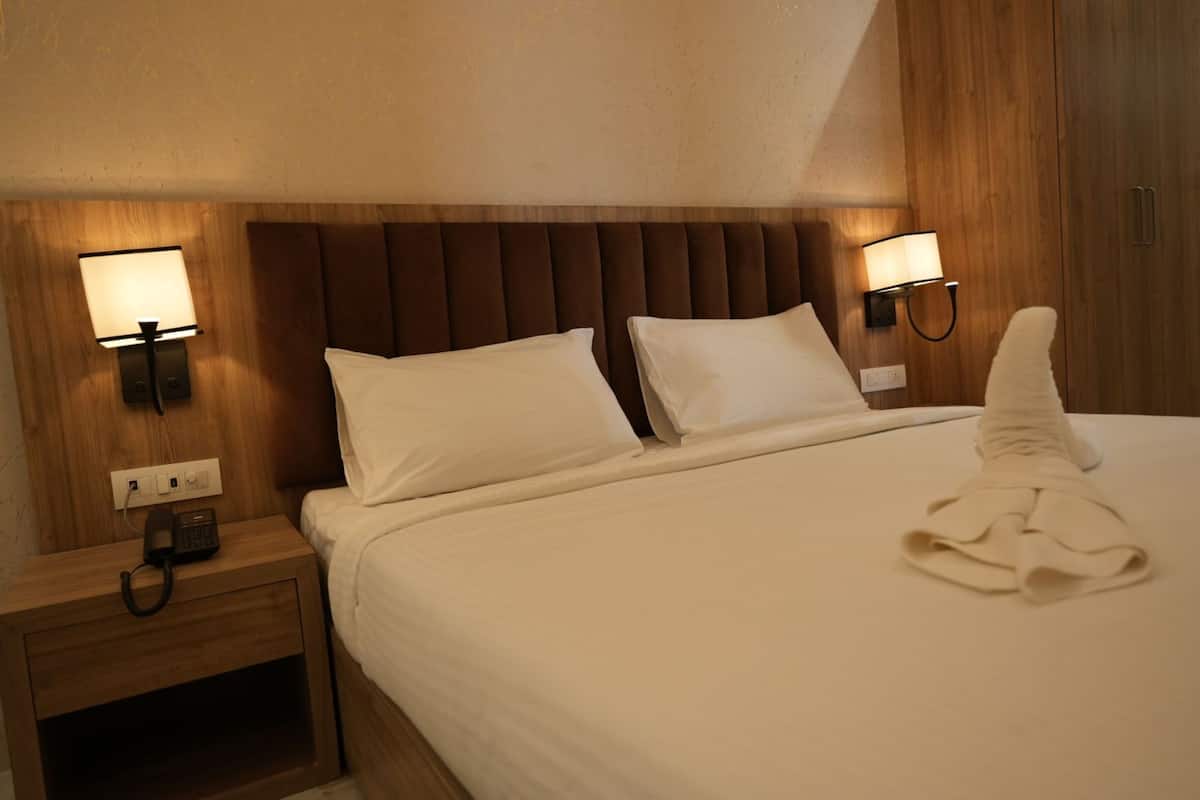 Une chambre d’hôtel avec un grand lit, deux lampes de chevet, une tête de lit en bois et une table de chevet avec un téléphone.