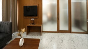 Ein modernes Wohnzimmer mit Flachbildfernseher an einer Wand aus Holzpaneelen, einer Couch, einem Couchtisch mit einer Vase und einer Schiebetür zum Balkon.