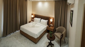 Ein Hotelzimmer mit einem großen Bett, zwei Nachttischen mit Lampen, einem Sessel, einem kleinen Tisch mit Pflanze und einer Deckenleuchte.
