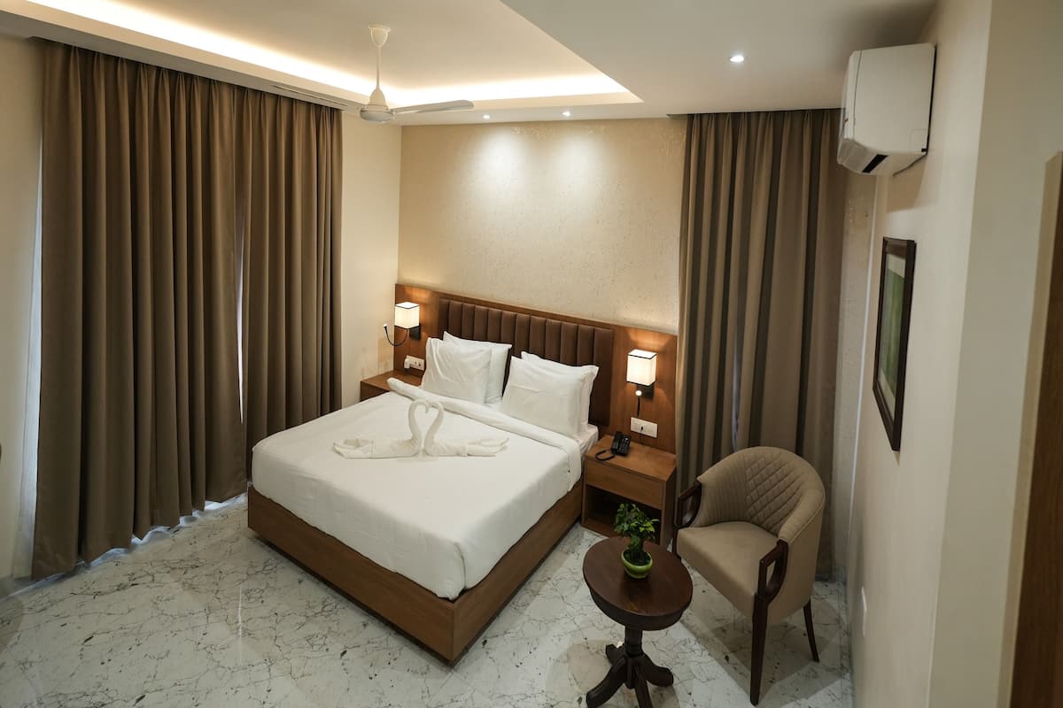 Une chambre d’hôtel avec un grand lit, deux tables de chevet avec des lampes, une chaise, une petite table avec une plante et un luminaire au plafond.