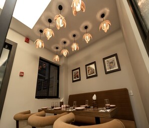 A dining area with a high ceiling, pendant lights, framed artwork, and a window.