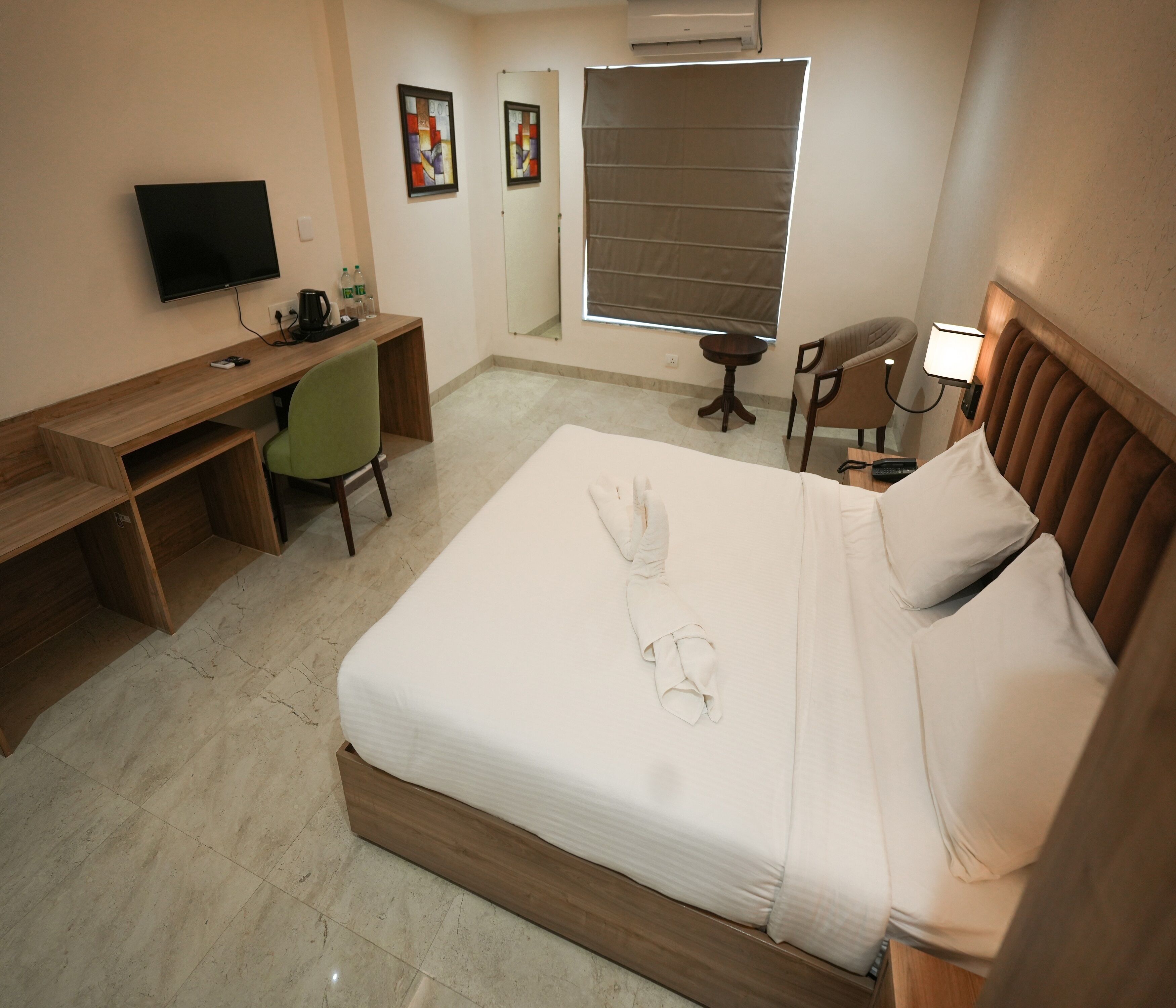 A hotel room with a bed, a desk, a chair, a TV, and a window with blinds.
