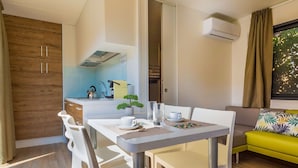 A modern kitchen with white cabinets, a dining table with chairs, a small plant, and a window with curtains.