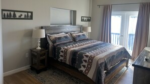 A bedroom with a bed, two bedside tables with lamps, a ceiling fan, a window with curtains, and wall art.