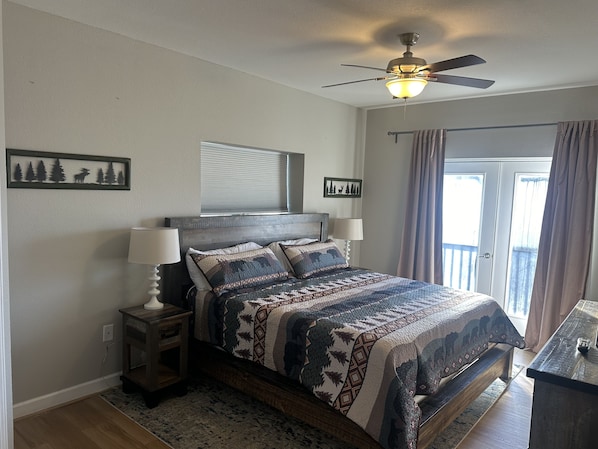 A bedroom with a bed, two bedside tables with lamps, a ceiling fan, a window with curtains, and wall art.