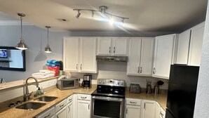 A modern kitchen with white cabinets, stainless steel appliances, and a tiled floor.