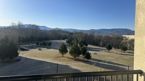A balcony with a view of a park, a car, and distant mountains.