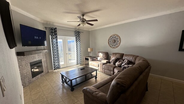 A living room with a brown leather sofa, a coffee table, a TV mounted on the wall, a fireplace, and a ceiling fan.