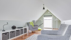 Un loft modern amb sostre alt, una taula cònsola blanca amb cistos, un armari gris, una làmpada de peu i vista exterior a través d'una finestra gran.