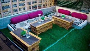 An outdoor seating area with cushioned benches and wooden tables, some with decorative vases. - Zaildar's Royal Garden Turtuk (Leh)