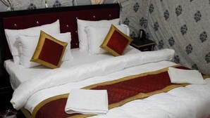 A neatly made bed with white and red bedding, a dark headboard, and a patterned wall. - Zaildar's Royal Garden Turtuk (Leh)
