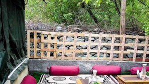 A cozy outdoor seating area with a wooden lattice wall, cushioned benches, and a patterned rug. - Zaildar's Royal Garden Turtuk (Leh)