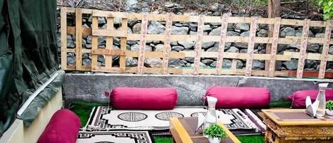 A cozy outdoor seating area with a wooden lattice wall, cushioned benches, and a patterned rug.