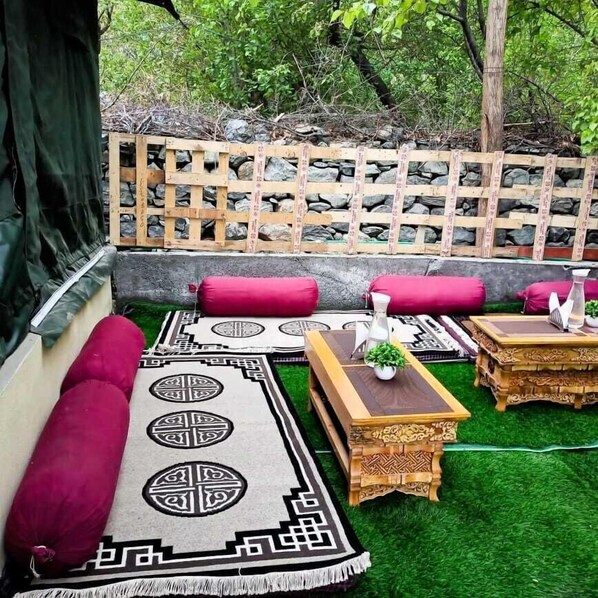 A cozy outdoor seating area with a wooden lattice wall, cushioned benches, and a patterned rug.