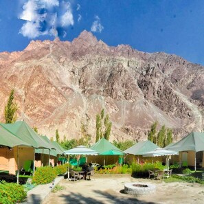 A row of tents with outdoor seating, set against a mountainous backdrop.