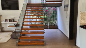 A spacious living area with a wooden staircase, a mounted TV, and a view of a balcony with flowers. - Sea and lake, sun and sand, history and geography we offer you with family warm. (Köyceğiz)