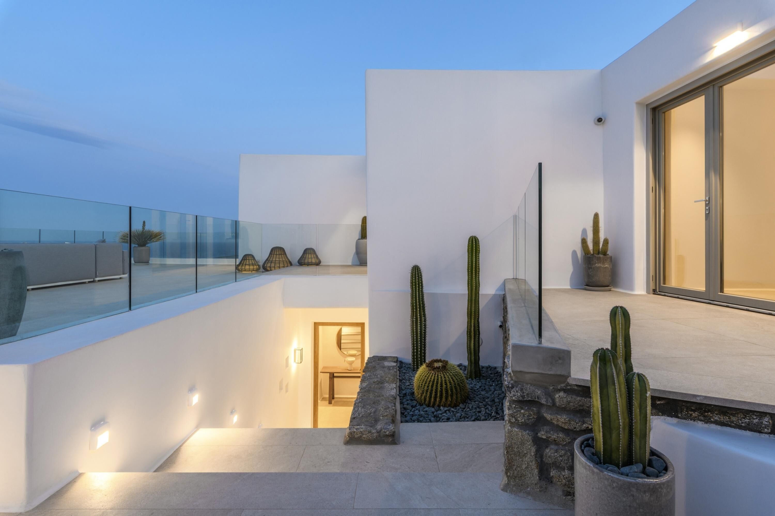Una terraza moderna al aire libre con barandas de vidrio, cactus y un sendero de piedra que lleva a una puerta.