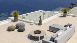 Una terraza en la azotea con vistas despejadas al mar, amueblada con un sofá, mesas redondas y plantas en macetas.