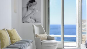 Un salon moderne avec un canapé et un fauteuil, une grande fenêtre donnant sur la mer et une photographie encadrée accrochée au mur.
