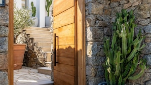 A stone wall with a wooden door leading to a staircase. - Channel I in Mykonos (Mykonos)