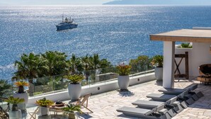 A rooftop terrace with a view of the sea, lounge chairs, and potted plants. - Channel I in Mykonos (Mykonos)