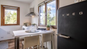 Cozinha moderna com bancada branca, geladeira preta e janela com vista para árvores.