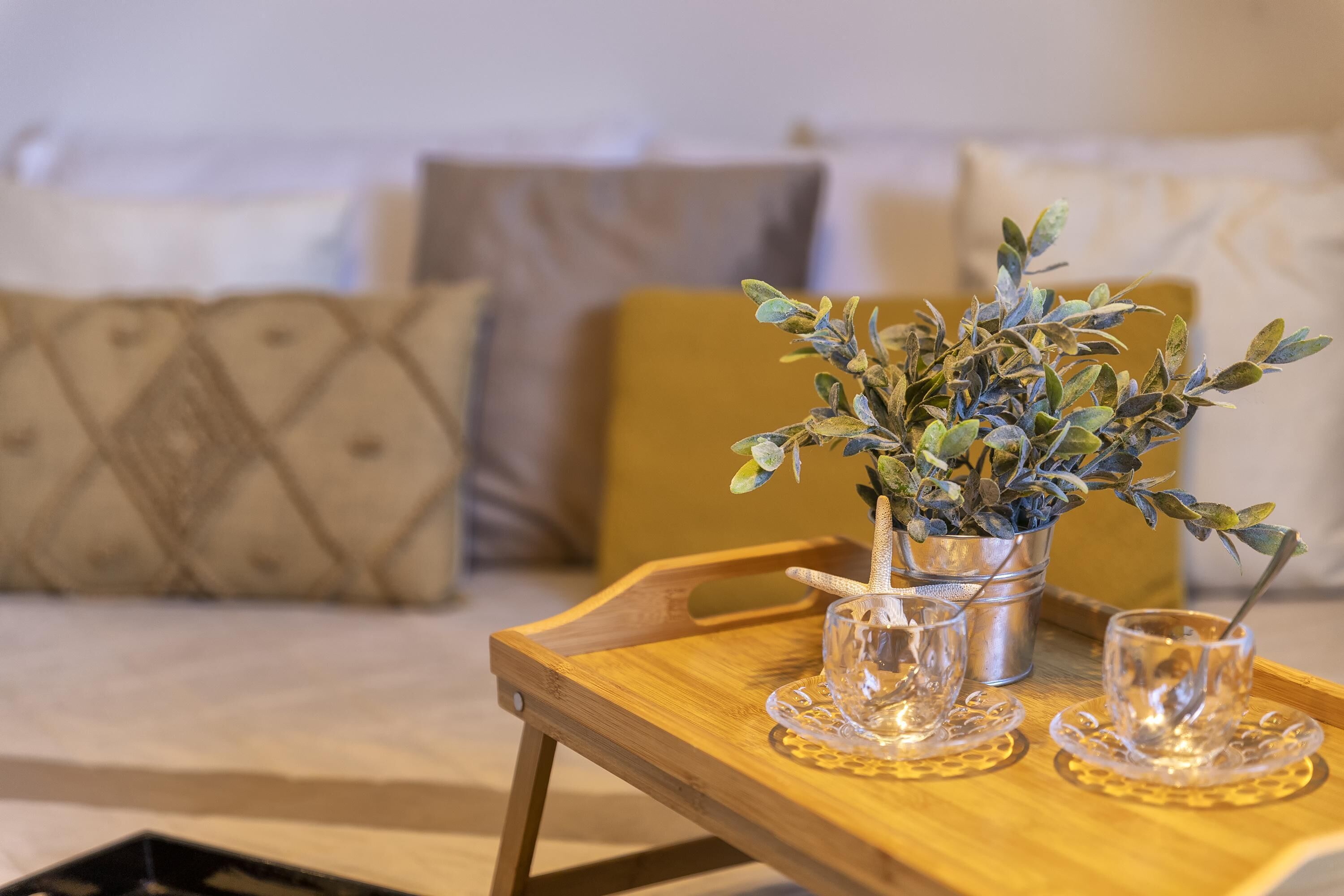 Un plateau en bois avec un seau en métal contenant une plante, deux verres transparents et une cuillère.