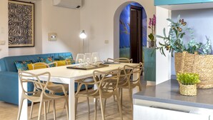 A modern living room with a dining area, featuring a sofa, chairs, a table, and decorative plants.
