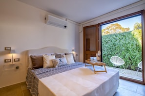 Une chambre à coucher comprenant un lit, des lampes de chevet, un appareil de climatisation et une vue sur la verdure, accessible par une porte-fenêtre coulissante.