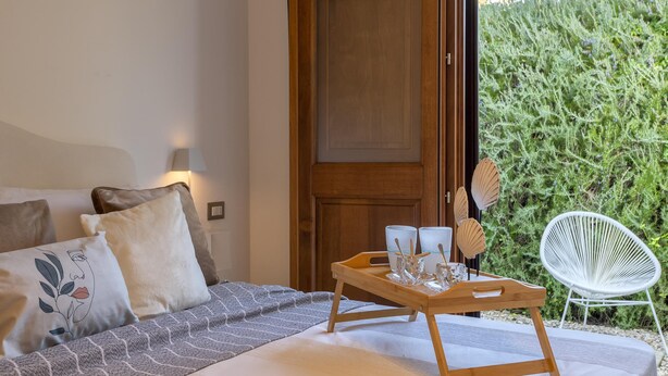 A bedroom with a bed, pillows, a bedside table with a tray, and a chair.