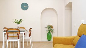 Un comedor con mesa y sillas, un reloj en la pared y un jarrón verde con plantas.