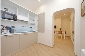 A modern kitchen with white cabinets, a microwave, and a sink. There is a dining area with a table and chairs visible through an open doorway. - Ottaviano Vatican Flat - Blue (Rome)