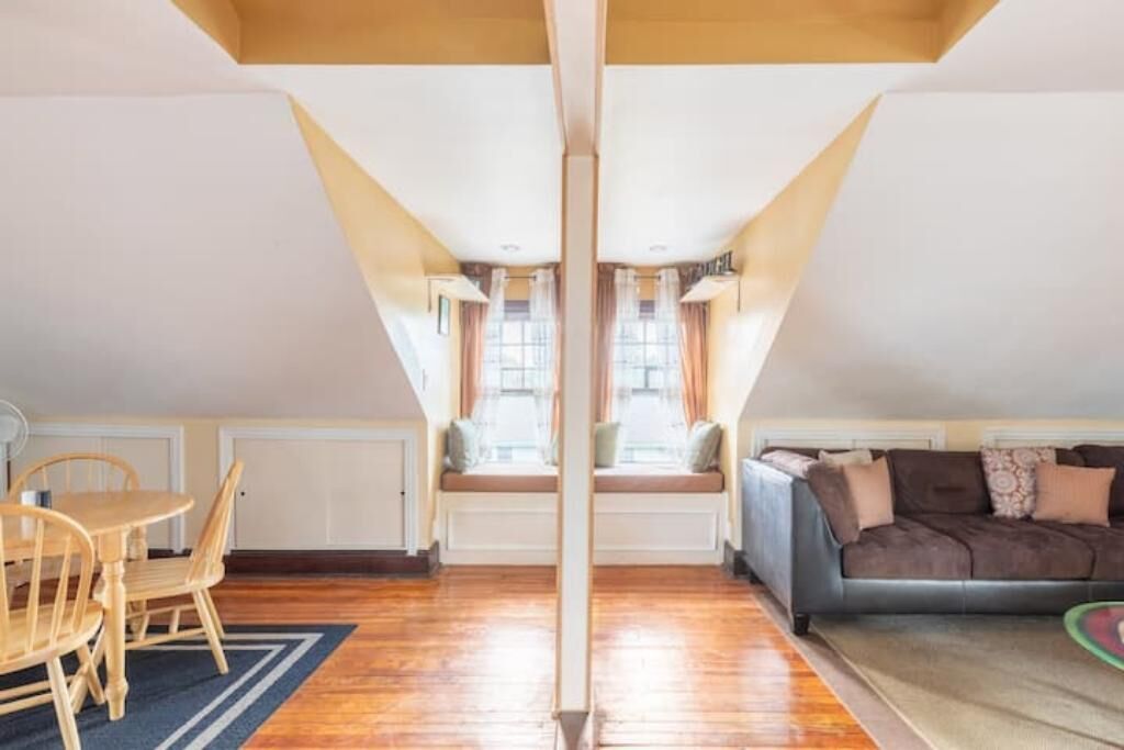A cozy attic room with a dining table, chairs, a sofa, and a window seat.