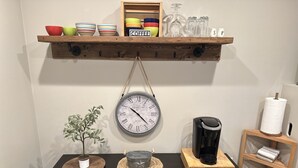 Un plan de travail de cuisine avec une machine à café, une horloge et une étagère contenant des bols et des verres.
