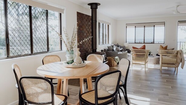 A spacious living area with a round wooden table, wicker chairs, and a stone fireplace. - Indooor & Outdoor Fireplace | Acreage | Ocean View | 10min to Australia Zoo (Mount Mellum)