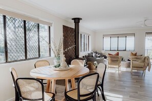 A spacious living area with a round wooden table, wicker chairs, and a stone fireplace. - Indooor & Outdoor Fireplace | Acreage | Ocean View | 10min to Australia Zoo (Mount Mellum)