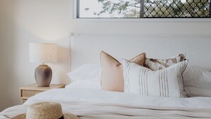 A neatly made bed with a straw hat, a lamp, and a window with a view of trees. - Indooor & Outdoor Fireplace | Acreage | Ocean View | 10min to Australia Zoo (Mount Mellum)