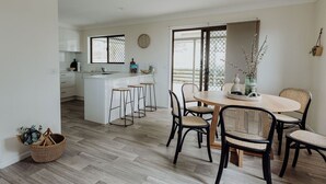 A modern kitchen with white cabinets, a central island with stools, and a dining area with a round table and chairs. - Indooor & Outdoor Fireplace | Acreage | Ocean View | 10min to Australia Zoo (Mount Mellum)