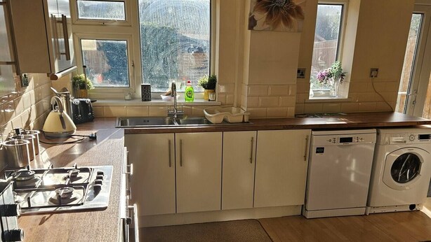 A modern kitchen with wooden flooring, a gas stove, a built-in dishwasher, and a window with a view of a snowy landscape. - 5-Bed House with separate living room (Birmingham)