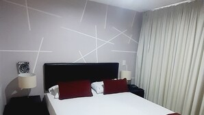 A hotel room with a large bed, two bedside tables, a nightstand, a wall with geometric patterns, and a window with curtains. - Aparta Estudio Loft (Bucaramanga)