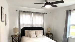 A bedroom with a bed, two bedside tables, a ceiling fan, and a window with curtains. - Pekin Cottage (Pekin)